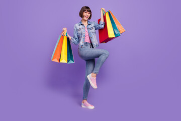 Full size photo of funny millennial brunette lady hold bags wear spectacles jeans shirt isolated on purple background