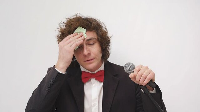 a nervous and shy Caucasian, a speaker with a microphone, a student is afraid to speak in front of a crowd of people or an audience. A young man wipes sweat from his forehead, isolated background