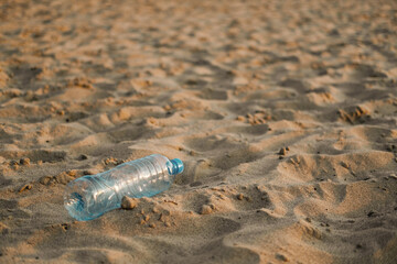 An empty plastic bottle is thrown onto a sandy beach. Environmental problem of plastic waste pollution.