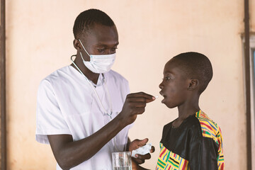 Young black medical trainee with face mask administering a tablet to a cute and compliant African...
