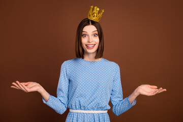 Photo of impressed young brunette lady hold empty space wear crown blue shirt isolated on brown...