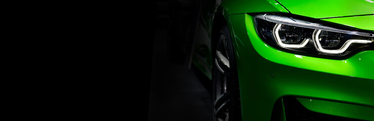 Front headlights of green modern sport car on black background, free space on left side for text. - obrazy, fototapety, plakaty