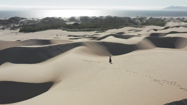 Woman uses a virtual reality headset and joysticks, dancing on sand dunes 4K