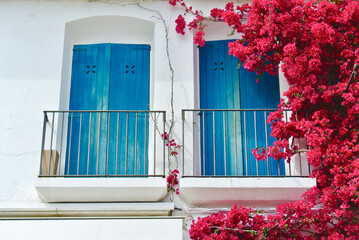 Vivid pink Bougainvillea flowers hanging around balcony with blue doors in Calella de Palafrugel,...