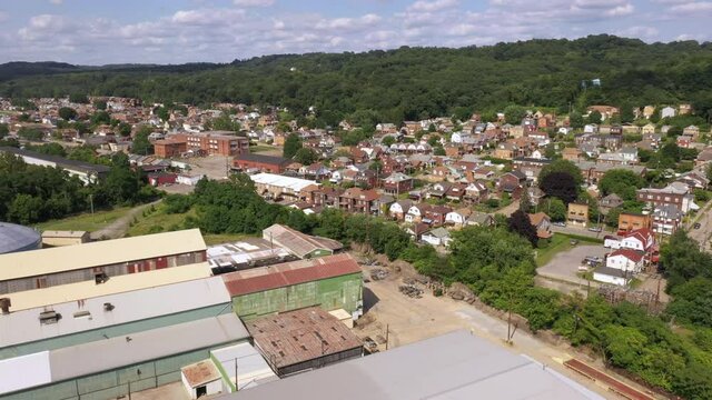 A daytime summer aerial establishing shot view of a typical western Pennsylvania small town. Steel mill, warehouse, or factory in the foreground, homes in the distance. Pittsburgh suburbs.	