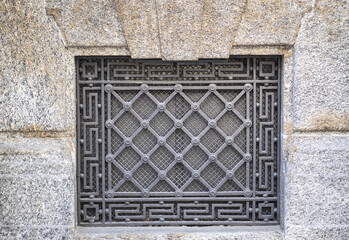 wrought iron grate with geometric decorations on the stone facade of a building