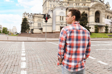 Young man waiting to cross street, back view. Traffic rules and regulations