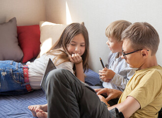 Obraz premium brother, sister and dad are sitting on the bed with a laptop and discussing. The concept of a family holiday