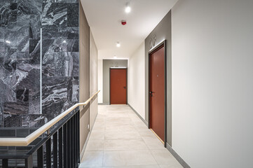Staircase of modern apartment building. White walls with marble decorations. Metalic railings and tile floor. Clean look.