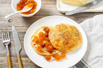 Homemade Danish buns with poppy seeds with butter and cherry jam in a white plate on a light gray wooden kitchen table closeup. Delicious traditional Scandinavian pastries for breakfast