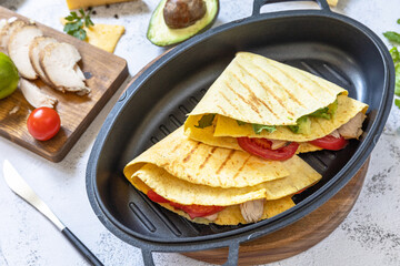 Sandwich chicken Mexican corn tortillas with avocado, arugula and cheese on a gray stone tabletop.
