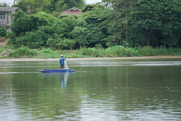Lonely man stands on the boat and collects the fish from the net with forest in background.