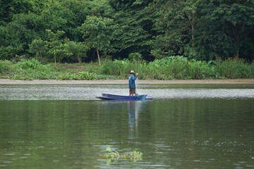 Fototapeta na wymiar Lonely man stands on the boat and collects the fish from the net with forest in background.