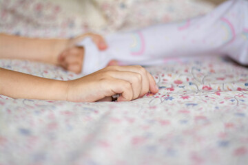 Obraz na płótnie Canvas The child's hand lies on the bed on a light background.