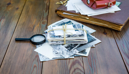 A stack of old photographs, a photo album, a film camera in a leather case on a wooden table