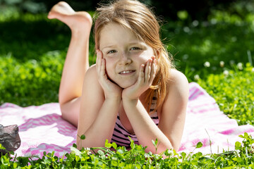 little girl with freckles lies and sunbathes on the grass in summer