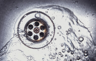 Water drains down on stainless steel kitchen sinkhole. Top view sewer in the washbasin. Household plumbing. Cleaning and hygiene concept.