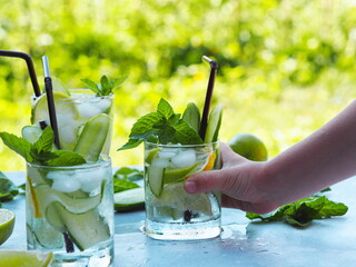 A child is hand takes a summer cold drink with ice, cucumber, lemon and lime to cool in the heat.