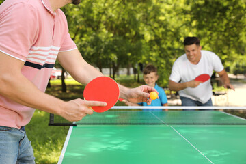 Family with child playing ping pong in park, closeup - obrazy, fototapety, plakaty