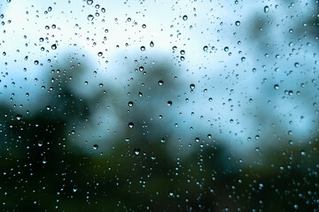 Rain droplets on surface of car glass with blurred green nature background through window glass of the car covered by raindrops. Freshness after rain. Wet windscreen shot from inside car.