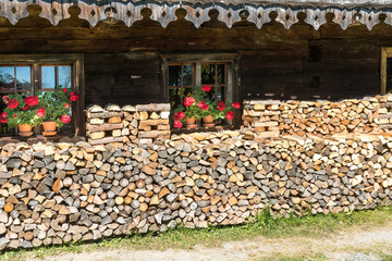Kaminholz und Fenster mit roten Geranien