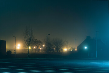 An empty car park with street lights glowing in the distance on a mysterious moody,  foggy atmospheric winters night