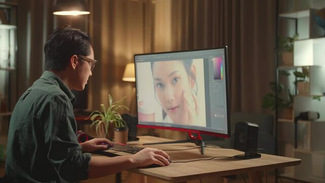 Tired Asian Male Digital Editor Works In Photo Editing Software On His Personal Computer With Big Display, He Works At Night 
