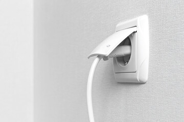 White electrical plug in the electric socket on a wall, interior photo