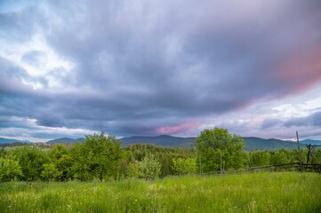 Obraz premium Evening in the mountains. Sunset. Cloudy sky of blue and pink or Very peri tones. Wooden fence. Summer time. Cloudy weather
