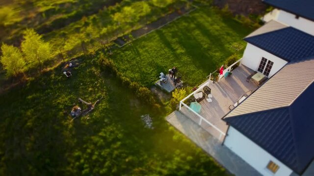 High angle drone shot of a house in small town with green yard where man is making barbecue. Aerial view of a cottage in countryside and male person is frying meat. Spending time in a village on dacha