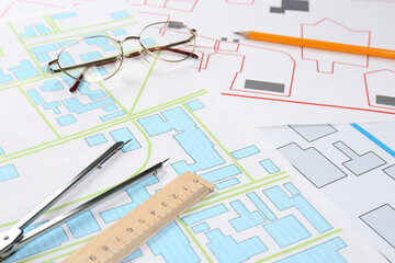 Office stationery and eyeglasses on cadastral maps of territory with buildings - obrazy, fototapety, plakaty