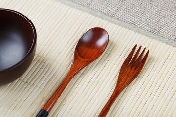 Empty dark wooden cup, spoon and fork made of natural wood on a light bamboo backing