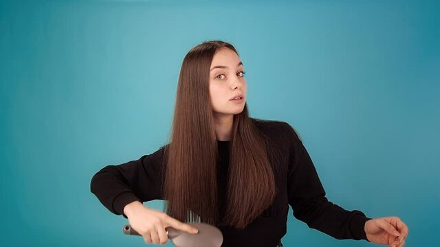 Lady model in black pullover brushes with hairbrush and looks at lost hair with shock in azure studio slow motion close view