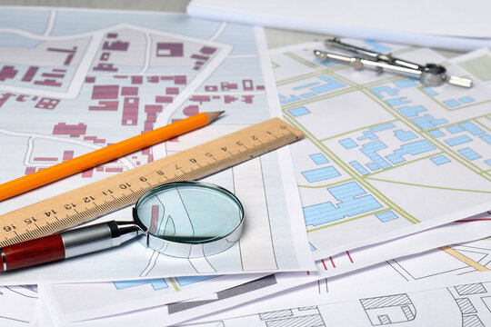 Office Stationery And Magnifying Glass On Cadastral Maps Of Territory With Buildings