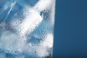 Naklejka na ściany i meble Ice cubes in a glass with refreshing ice water on a blue background.