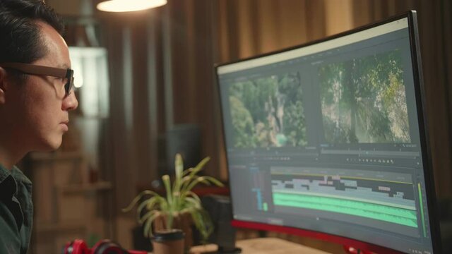 Tired Asian Male Video Editor Works With Footage And Sound On His Personal Computer, He Works Late At Night
