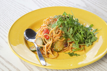 Spaghetti with vegetables and arugula served on yellow plate
