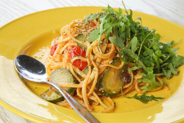 Spaghetti with vegetables and arugula served on yellow plate