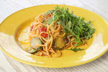 Spaghetti with vegetables and arugula served on yellow plate