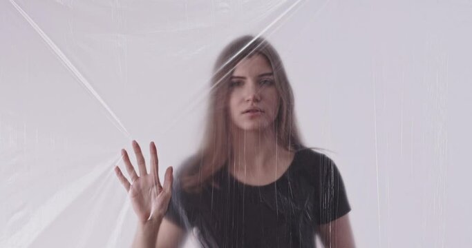 Sexism problem. Victim lifestyle. Woman harassment. Defocused worried confused female trapped behind clear polythene film isolated on light out of focus background.
