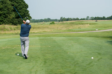 A golfer drives a ball from the tee on a links course.