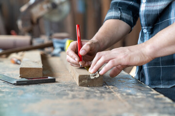 Male carpenter using pencil drawing sign on plank. Craftsman doing his job at the carpentry workshop