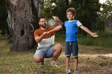 Man applying insect repellent on his son's arm in park. Tick bites prevention