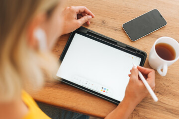 Young blonde woman in yellow t-shirt using digital tablet with cup of tea in the kitchen at home