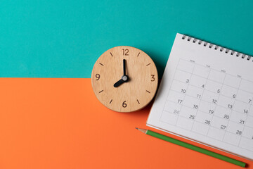 close up of calendar and alarm clock on the orange and green table background, planning for...