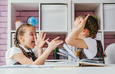 Two schoolgirls friends fool around during a lesson. Back to school concept. - obrazy, fototapety, plakaty