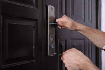 Handyman with screwdriver repairing door lock, closeup