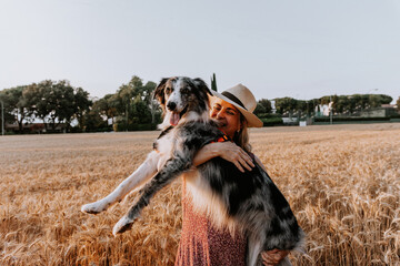 dog love. Adult woman hugging and holding her adorable border collie dog in a wheat fiel on summer.