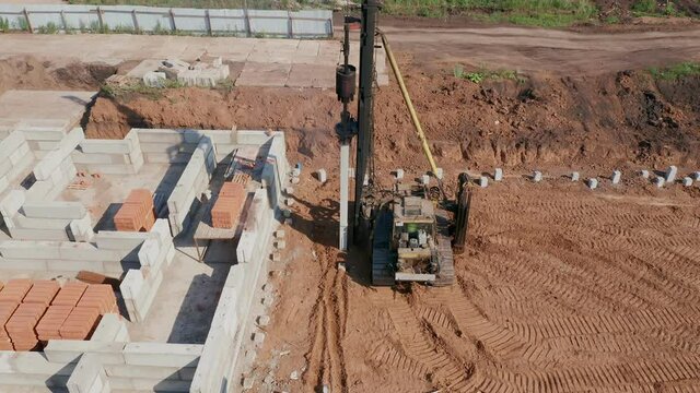 View of the sand trench in which construction equipment works. The process of laying slabs and blocks for the foundation of the building. Fence of corrugated board in the background. High quality.