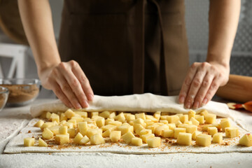 Woman making delicious apple strudel at table, closeup